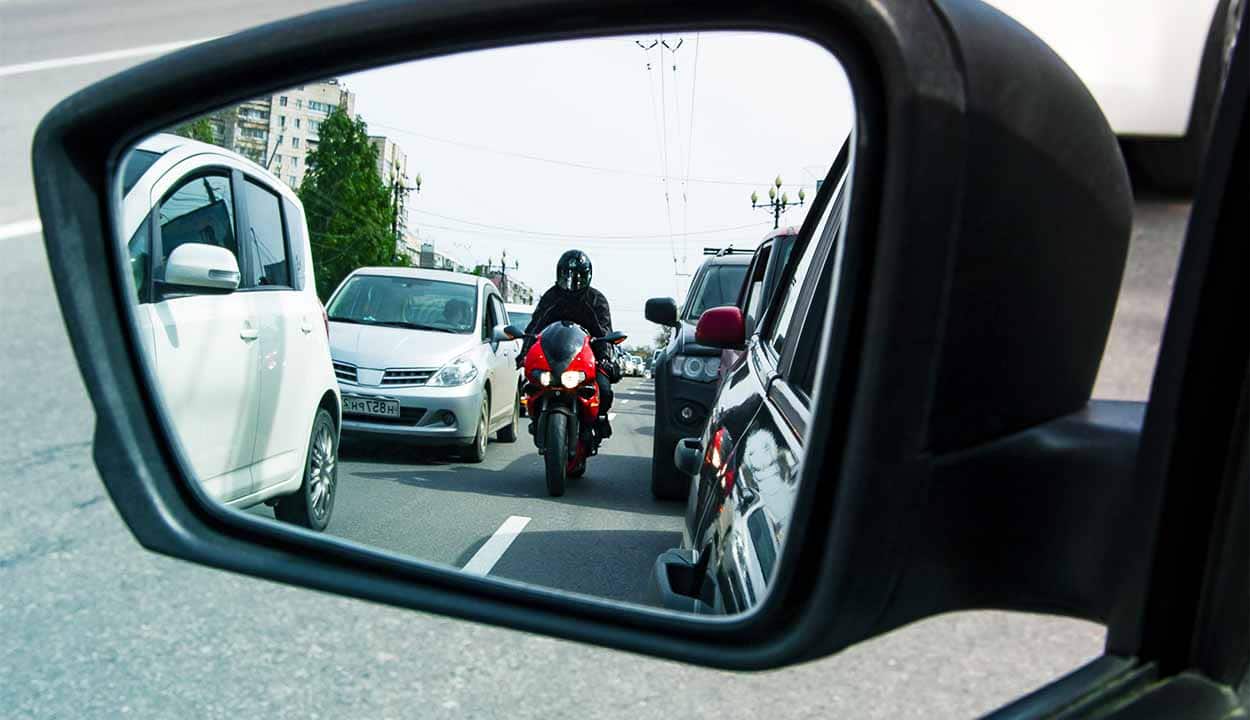Imagem do retrovisor de um carro onde é possível ver uma moto