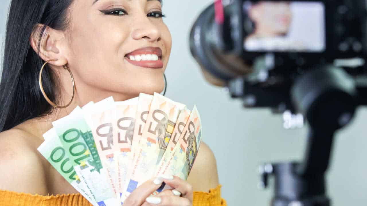 influencer feminina gravando vídeo e segurando notas de dinheiro em formato de leque