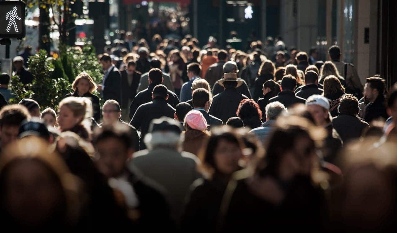 Visão ampla de uma multidão de pessoas caminhando em uma rua movimentada.
