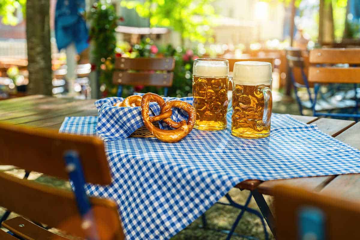 Mesa com toalha quadriculada azul e branca. Em cima, dois pretzels e duas canecas de cerveja