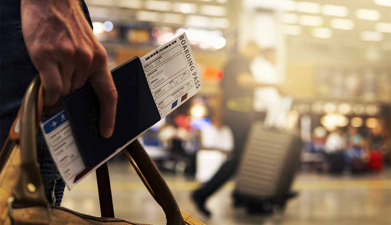 Closeup em uma pessoa segurando uma mala e passagens aéreas dentro de um aeroporto.