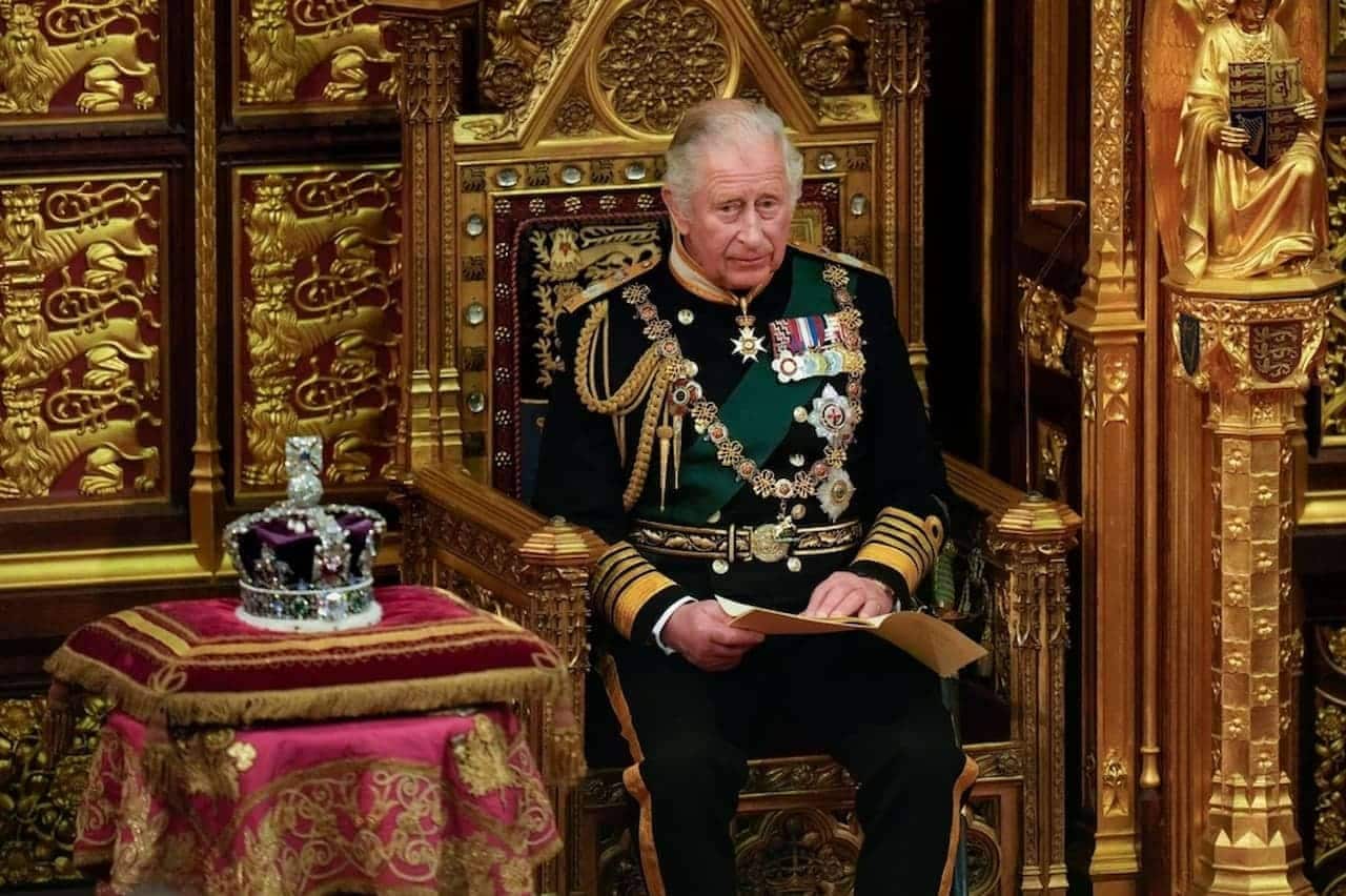 Príncipe Charles de farda sentado no trono