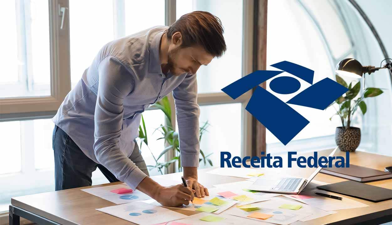 Imagem de um homem em frente a uma mesa com vários papéis espalhados, possivelmente trabalhando. No lado direito, aparece a logo da Receita Federal