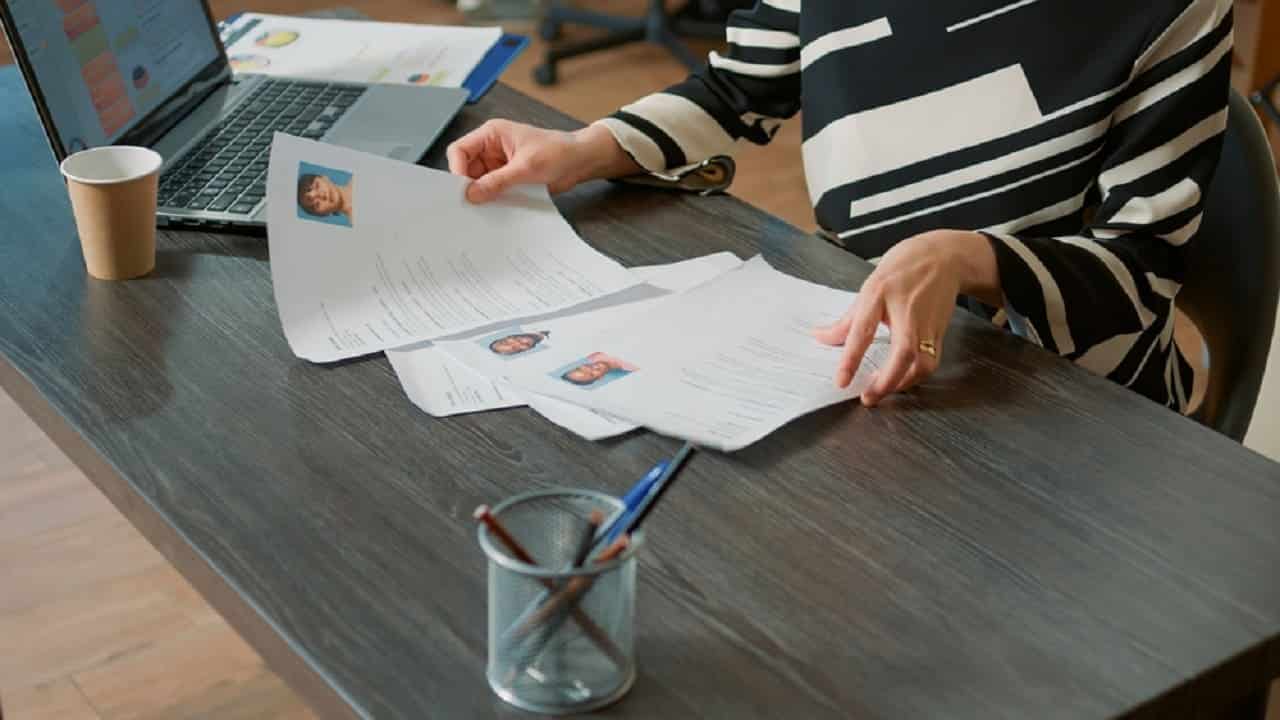 Imagem de uma mesa onde mãos analisam documentos.
