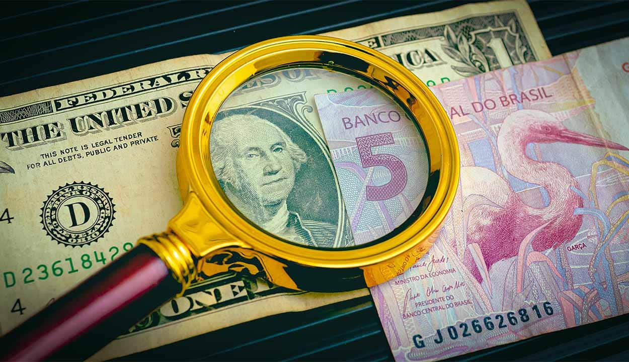 Lupa sobre duas notas de Real e Dólar