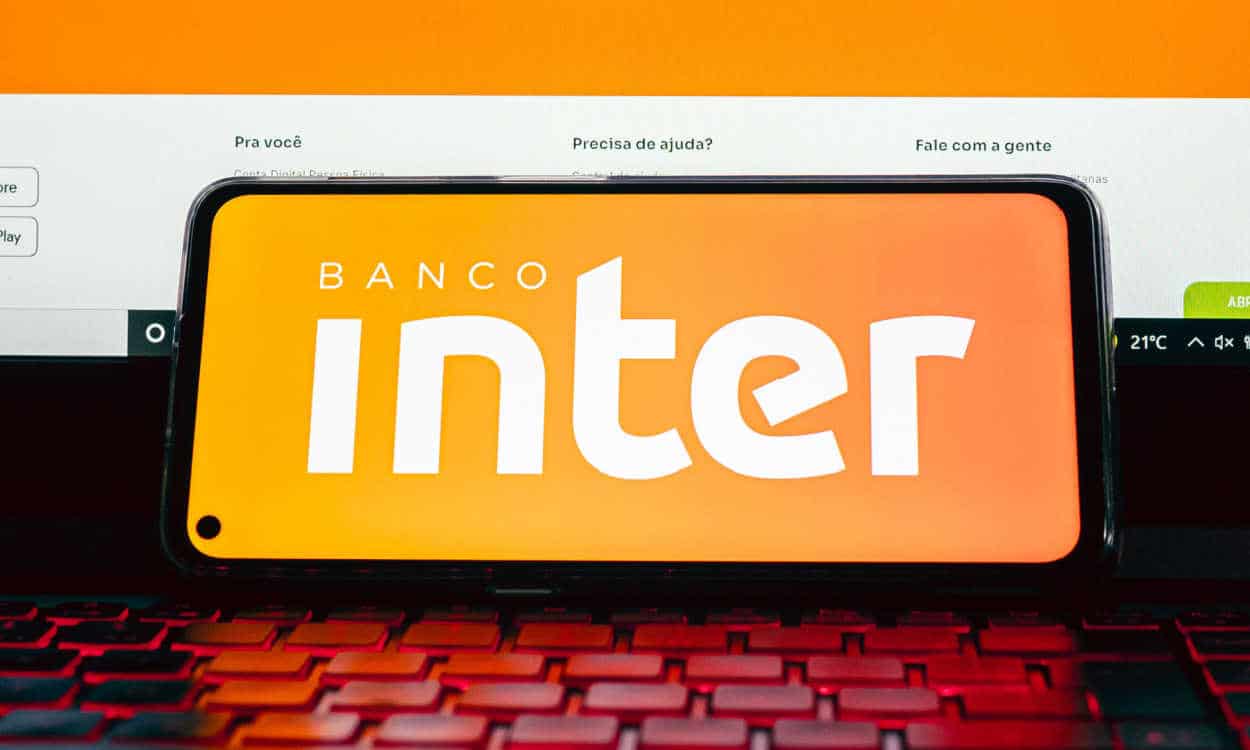 Celular com logo do Banco Inter na tela apoiado em um notebook