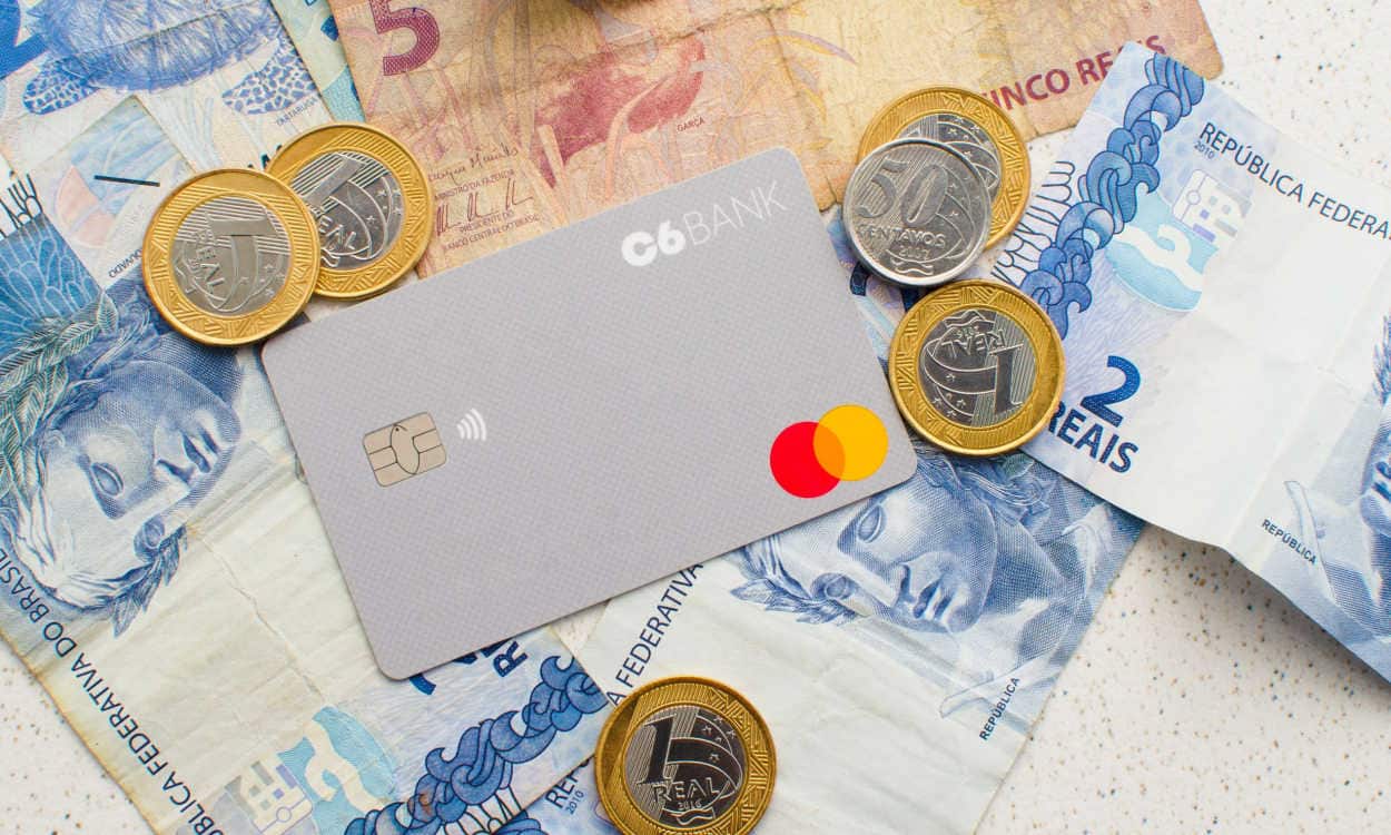 Cartão do C6 Bank com cercado de notas e moedas de Real