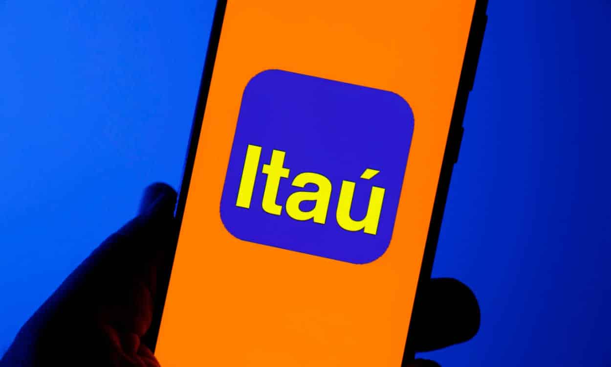 Imagem de pessoa segurando celular com a logo do banco Itaú na tela.