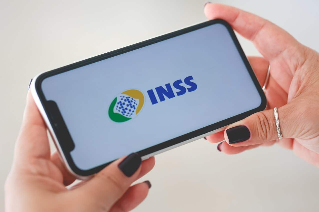 Mãos femininas segurando o celular aberto no aplicativo do INSS