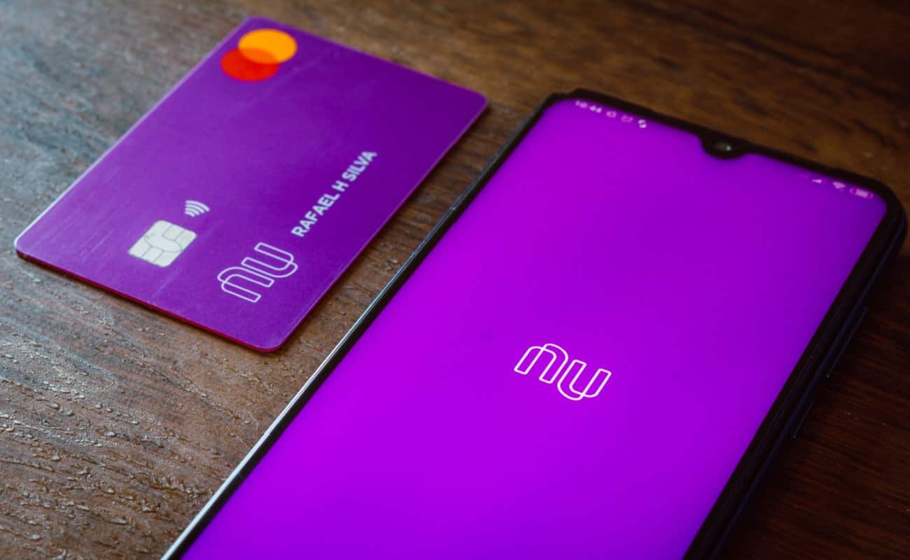 Celular com a logo do Nubank na tela ao lado de um cartão da fintech