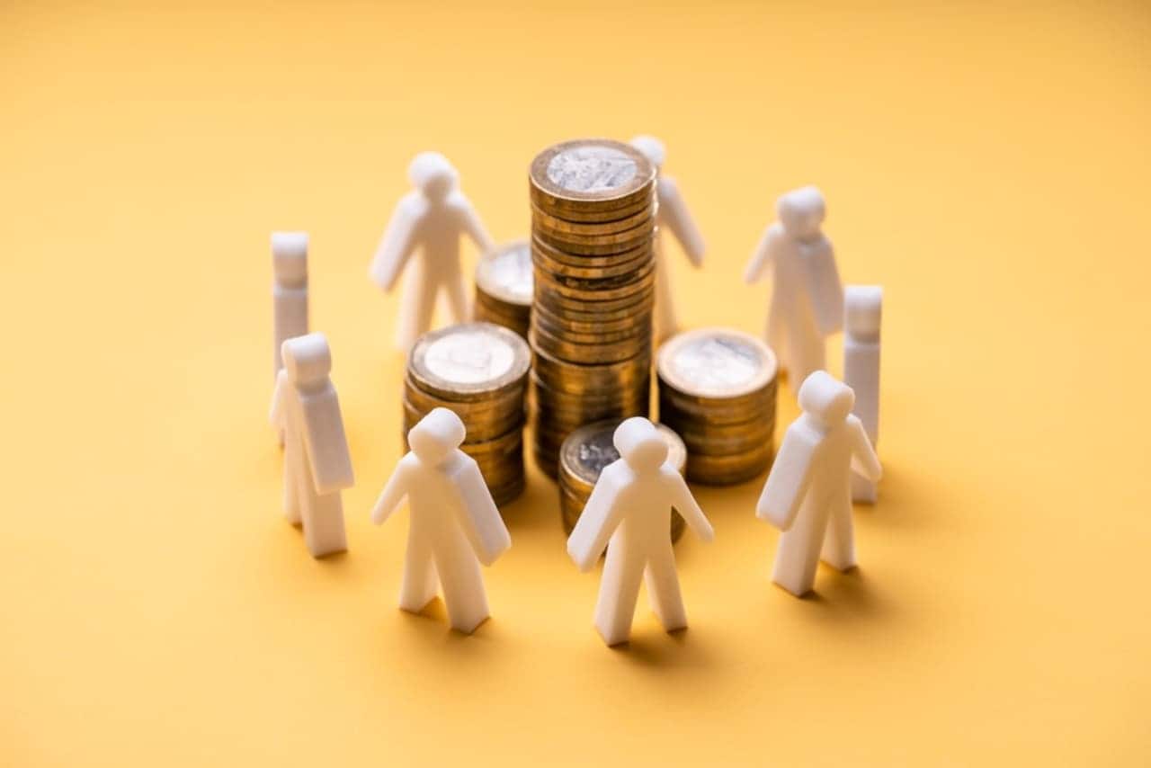 Miniaturas humanas em madeira fazendo uma roda em volta de pilhas de moedas