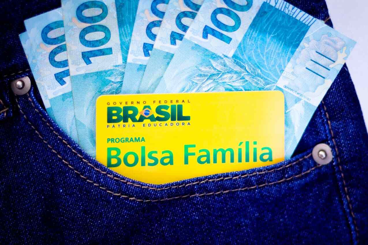 bolso de calça jeans com cartão do bolsa família e várias notas de cem reais.