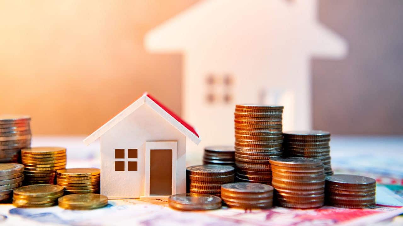Miniatura de casa e pilhas de moedas espalhadas ao redor