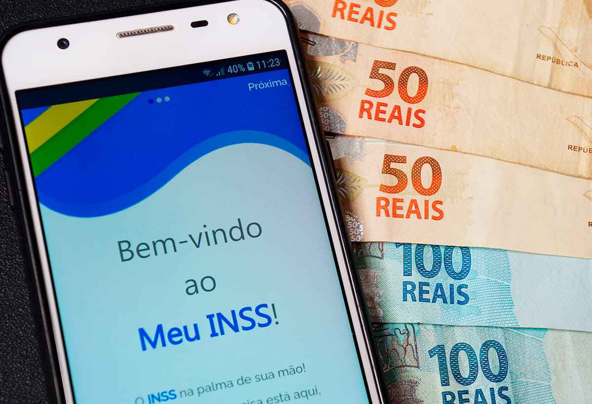 Aplicativo Meu INSS aberto no celular e notas de dinheiro ao lado