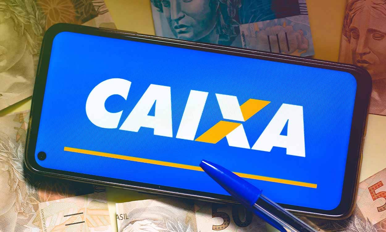 Ao lado de notas brasileiras e caneta azul, celular exibe logo da Caixa