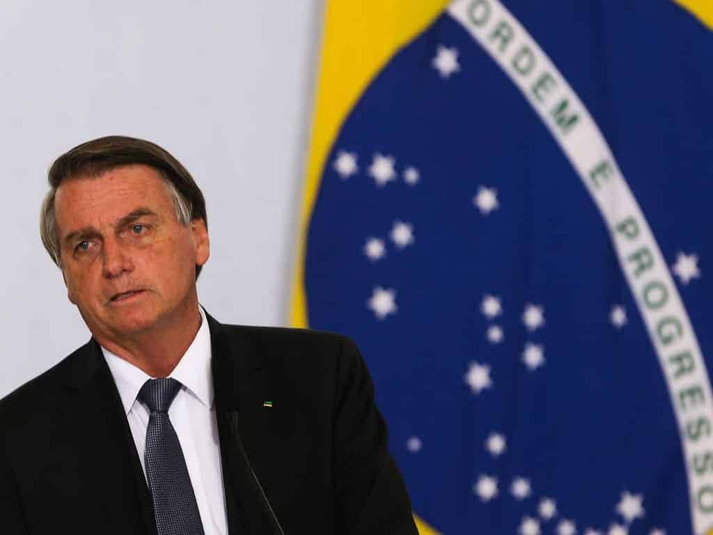 Imagem de Bolsonaro ao lado de uma bandeira do Brasil.