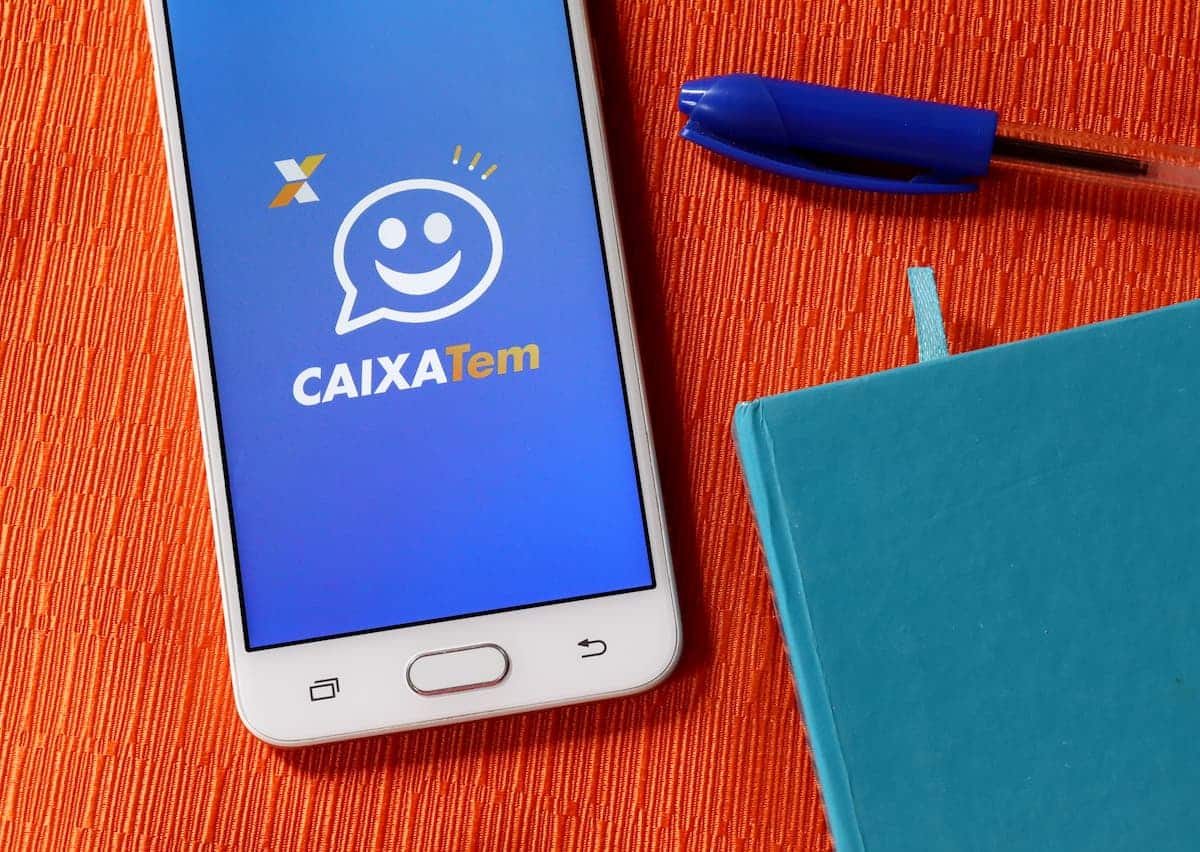 Aplicativo da Caixa Tem aberto em celular de cliente, em cima de mesa com materiais de escritório em sua volta.