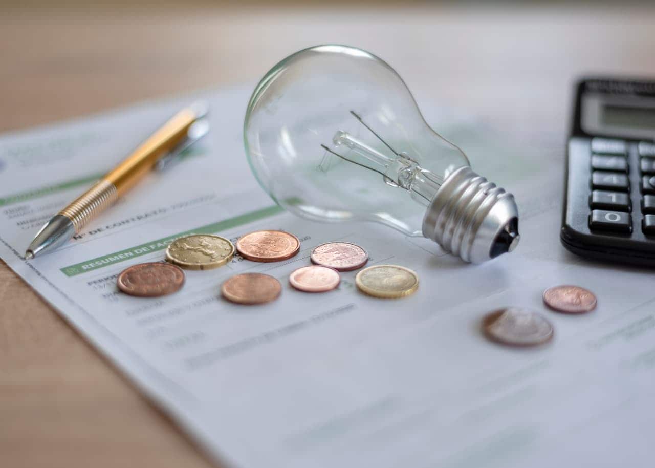 Lâmpada, moedas, caneta e calculadora em cima de uma conta de energia
