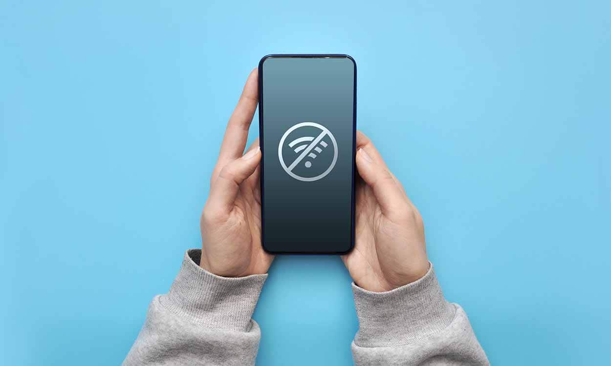 Imagem de mãos segurando um celular com a tela com símbolo do Wifi bloqueado.