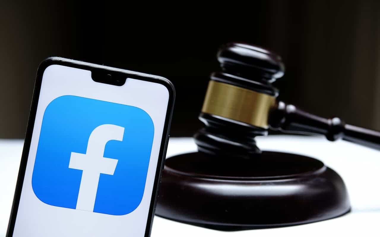 Em primeiro plano, um celular com logo do aplicativo Facebook. Ao fundo, um malhete, um martelo de juiz, utilizado em tribunais.