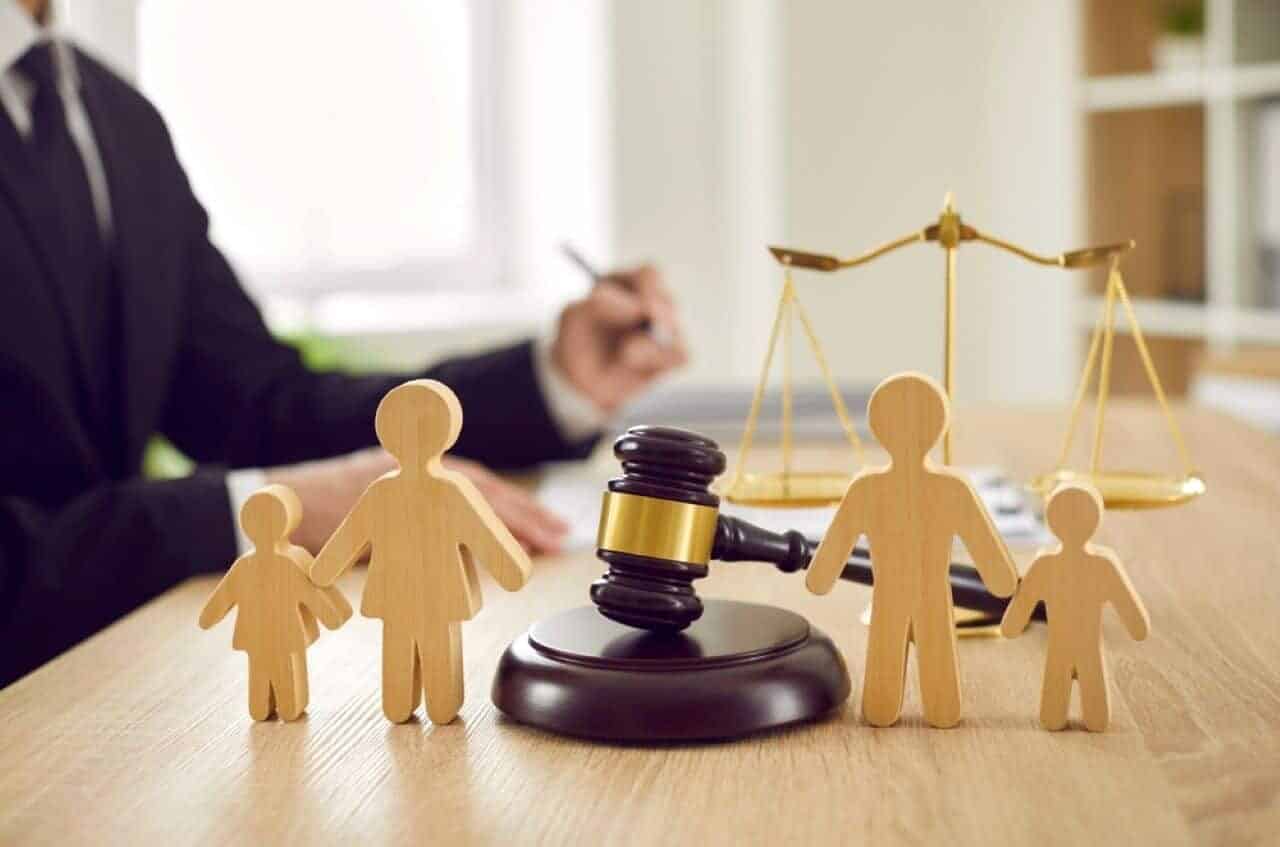 Mesa de escritório com bonecos de madeira que representam membros de uma família, um martelo de tribunal e uma balança da justiça pix pensão