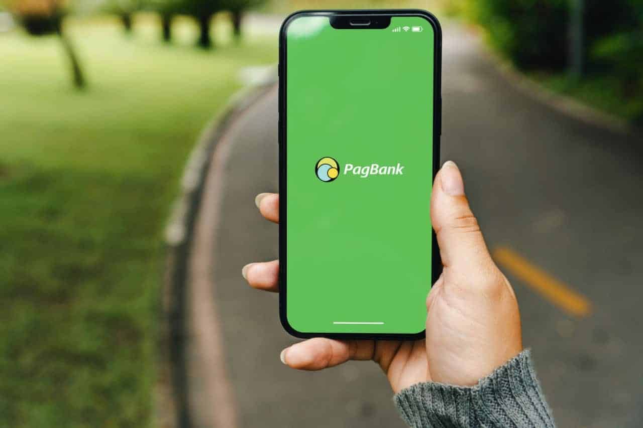 Mão segurando celular que mostra tela inicial do aplicativo PagBank
