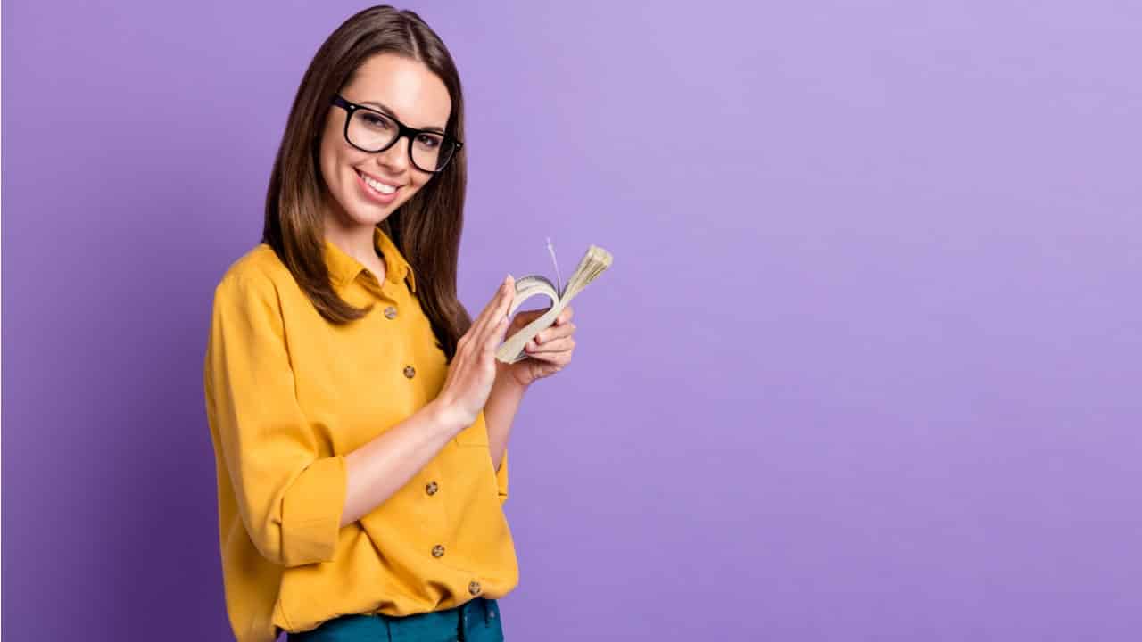 Mulher sorrindo segurando um maço de notas de dinheiro que ela mexe com outra mão