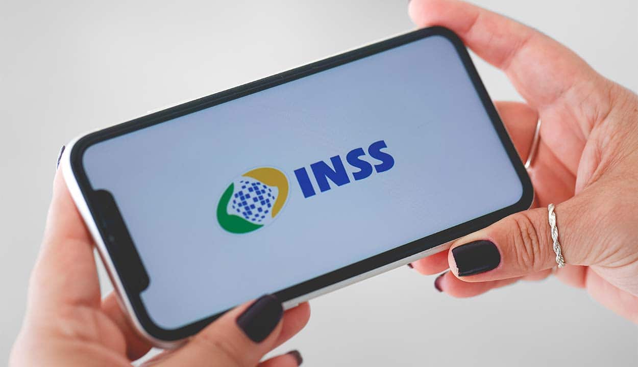 Mãos femininas segurando o celular aberto no aplicativo do INSS