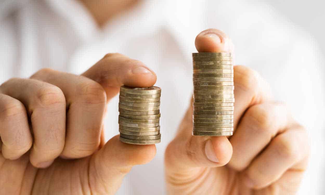 Pessoa segurando uma pilha de moedas entre os dedos. A pilha da mão direita é menor do que a esquerda