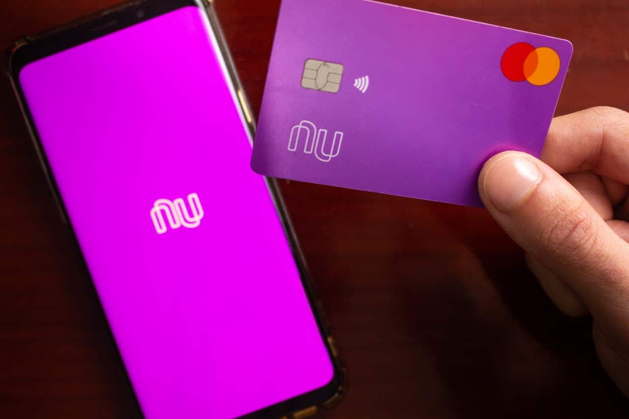 celular aberto no aplicativo do Nubank e uma mão segurando um cartão do banco
