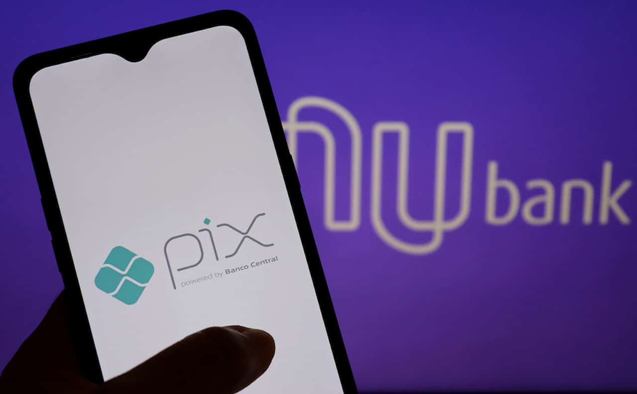 Mão segurando celular com o do Pix, logo do Nubank ao fundo