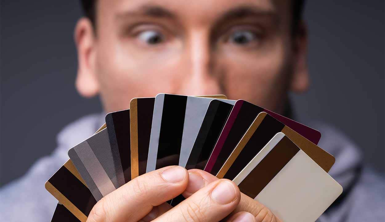 Homem desfocado olhando para um leque de cartões de crédito que ele segura em suas mãos. O foco está nos cartões.