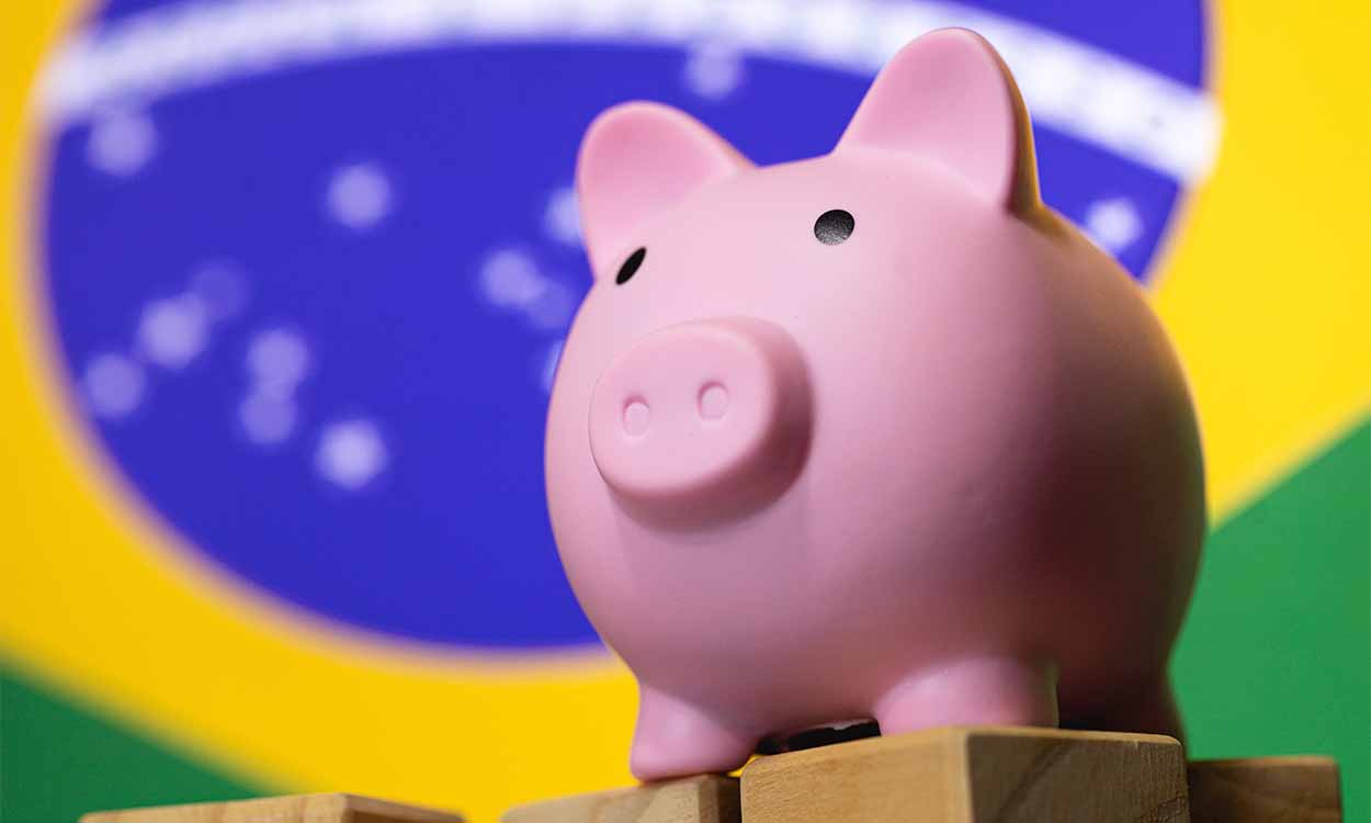 Brasil surpreende e lidera crescimento global no 1º trimestre Imagem de um cofre em formato de porco e uma bandeira do Brasil ao fundo atividade econômica