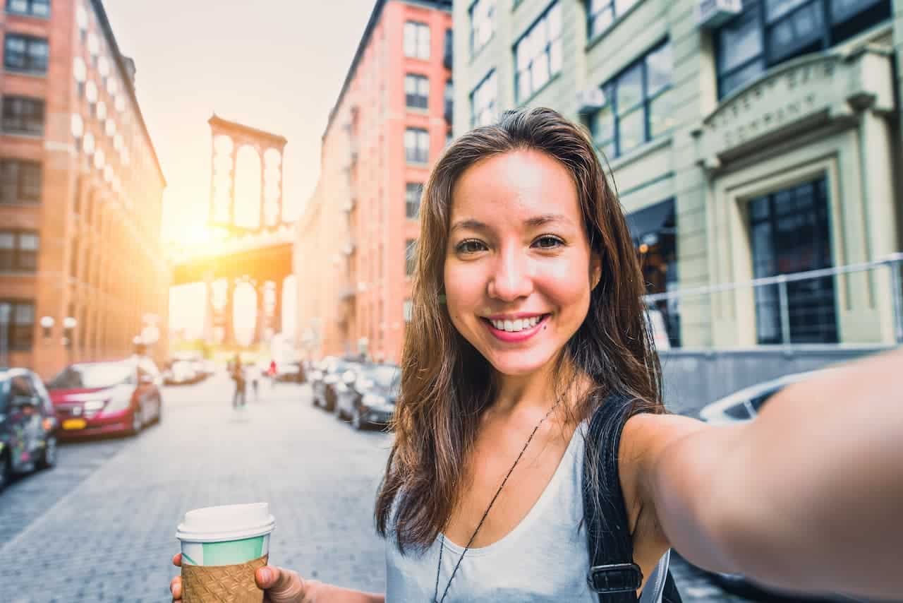 Mulher sorridente tirando selfie na rua enquanto segura café