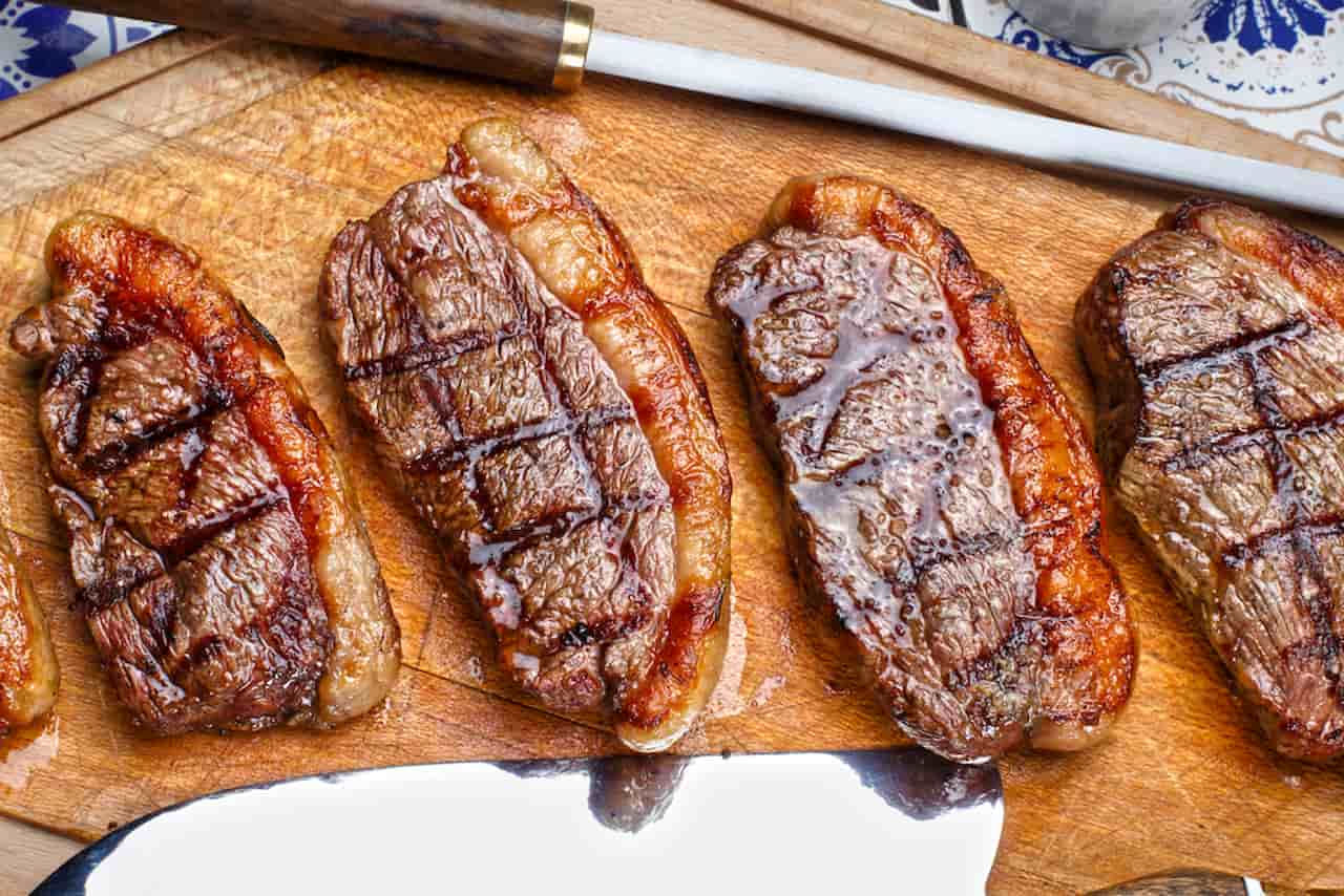 Quatro pedaços de picanha grelhada sobrepostos em uma tábua de carne.