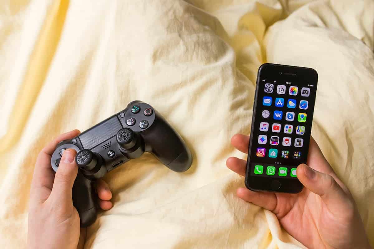 Pessoa segurando um controle de PS4 e iPhone.