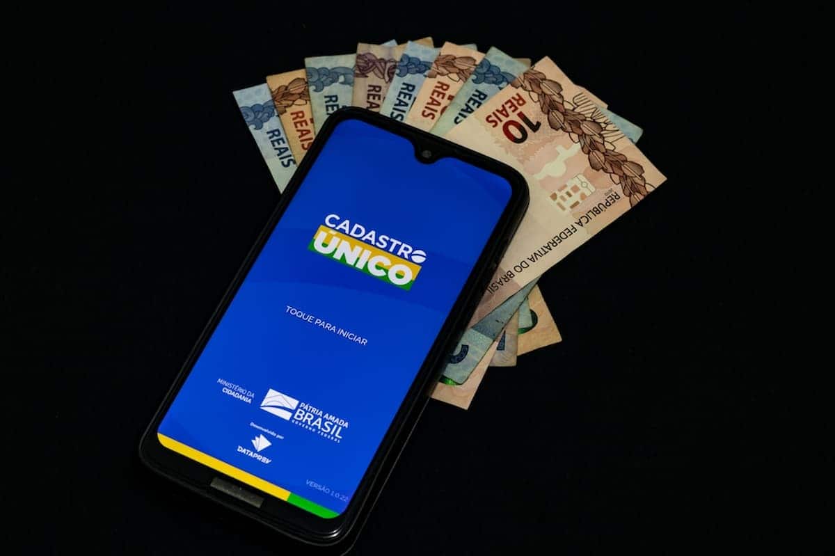 Celular em cima de cédulas de dinheiro, com o aplicativo do CadÚnico aberto