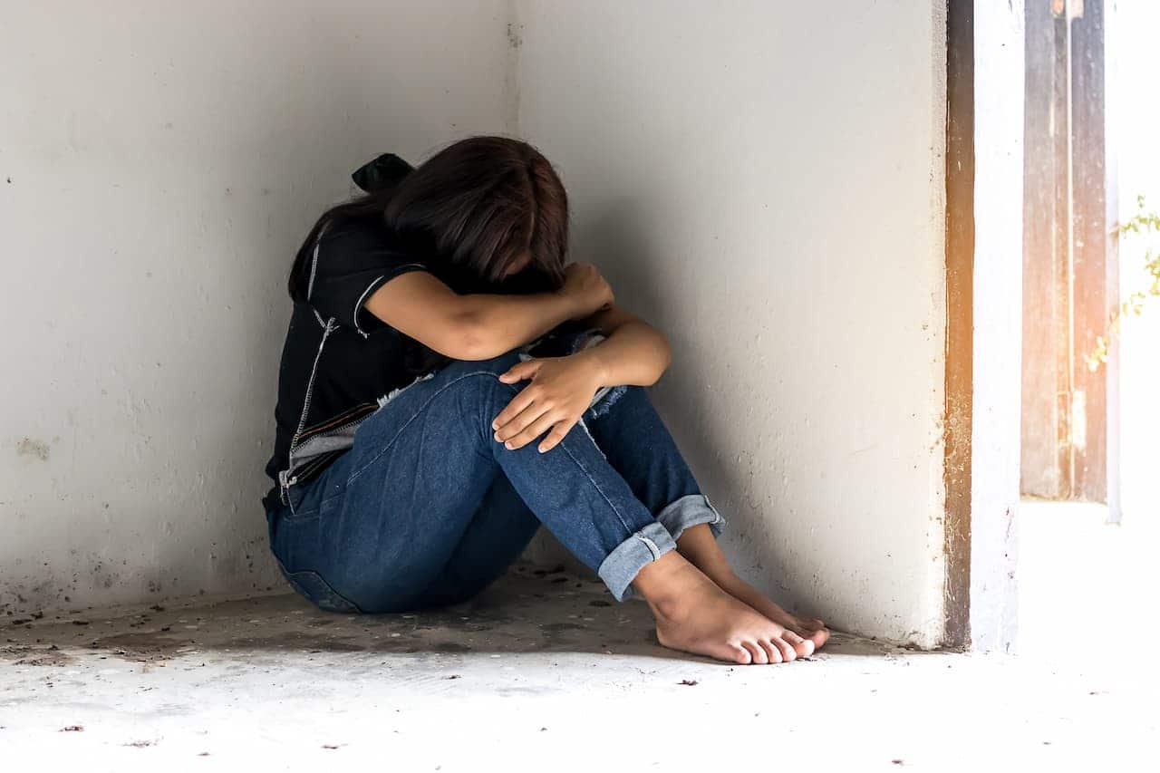Mulher acuada em um canto com a cabeça baixa