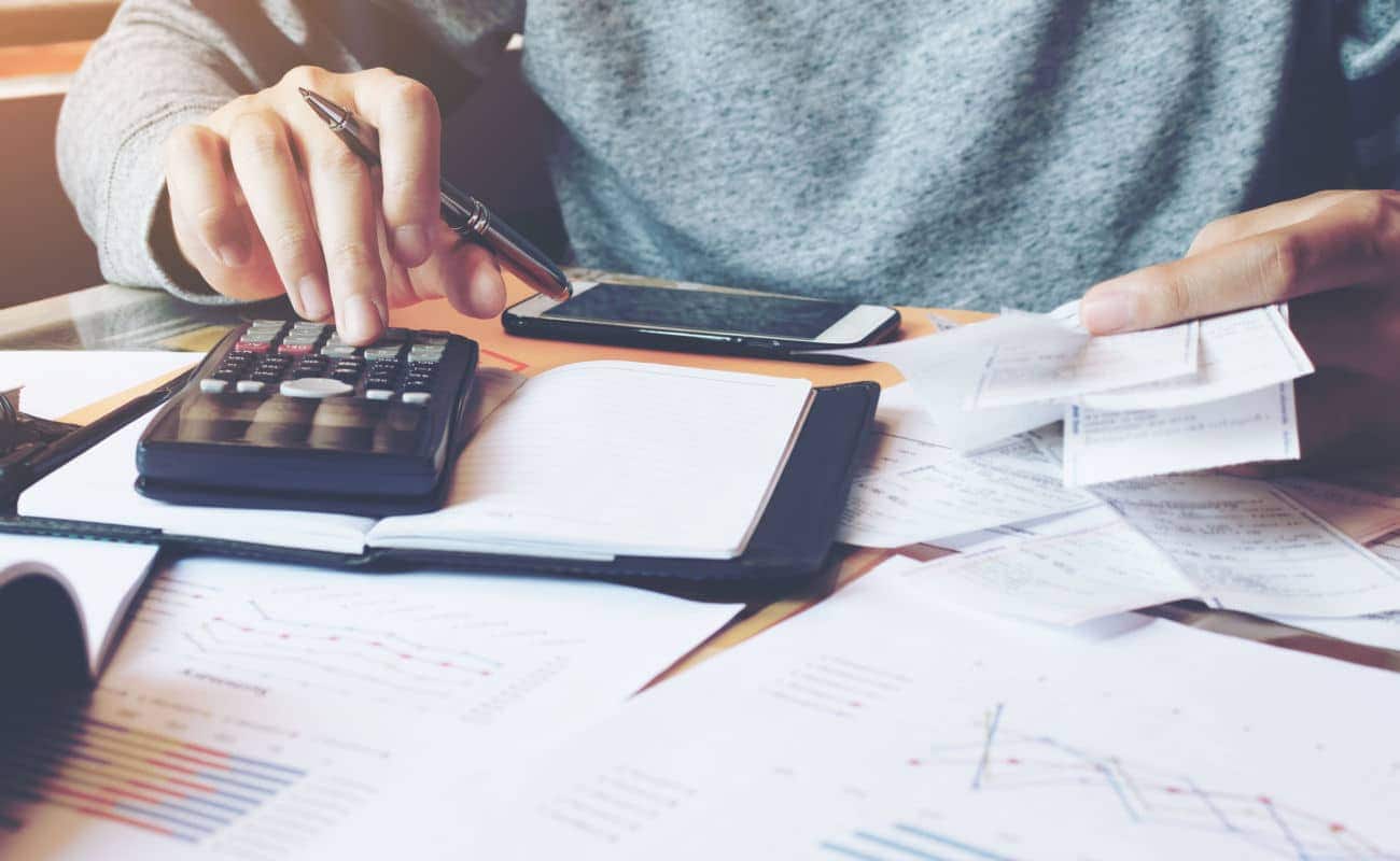 Pessoa usando uma calculadora e uma caneta, e com várias contas em cima da mesa