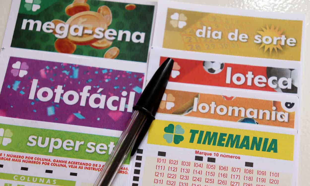 Caneta preta em cima de cartelas de várias modalidades das Loterias da Caixa