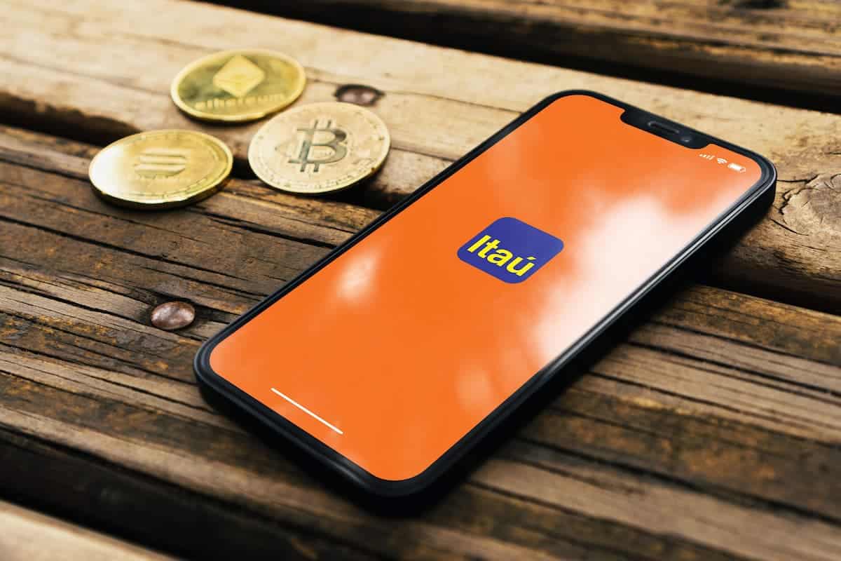 Aplicativo Itaú em celular com criptomoedas ao lado