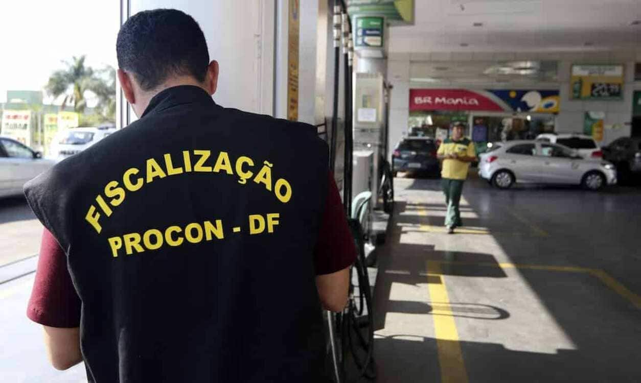 Agente do Procon em um posto de gasolina. Ele está de costas e olhando pra baixo. Na roupa que usa, dá pra ler "FISCALIZAÇÃO PROCON - DF" na parte de trás