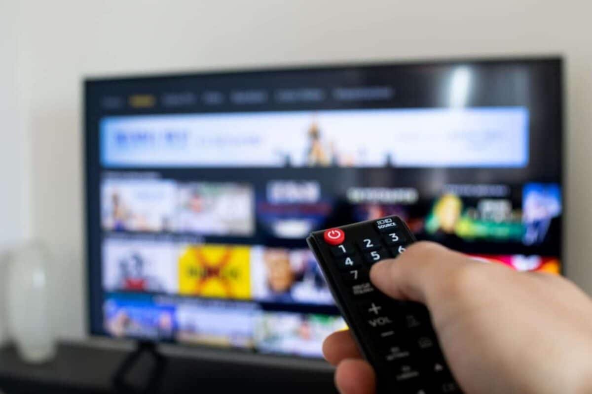 Mão segurando um controle remoto apontando para uma televisão com conteúdo fazendo referência ao TV Box