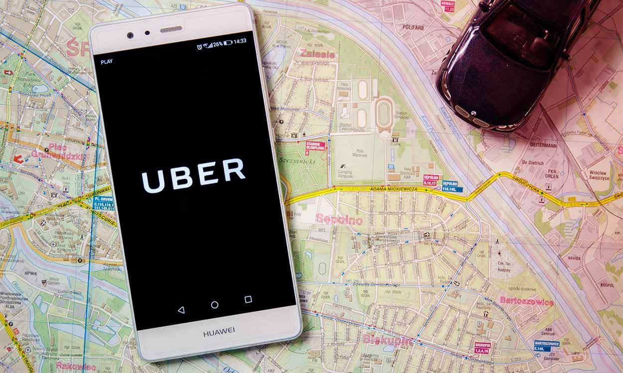 Celular com a logo da Uber na tela e uma miniatura de carro em cima de um mapa