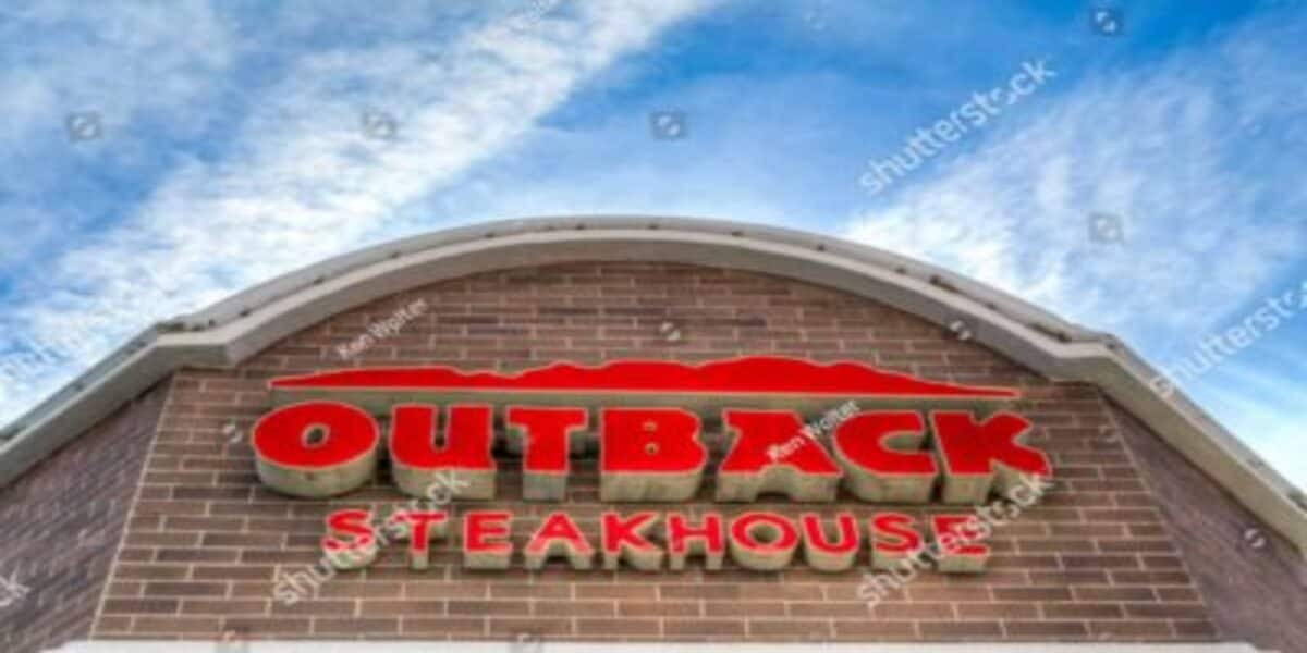 Fachada Outback com letreiro vermelho sobre tijolinhos e céu ao fundo.