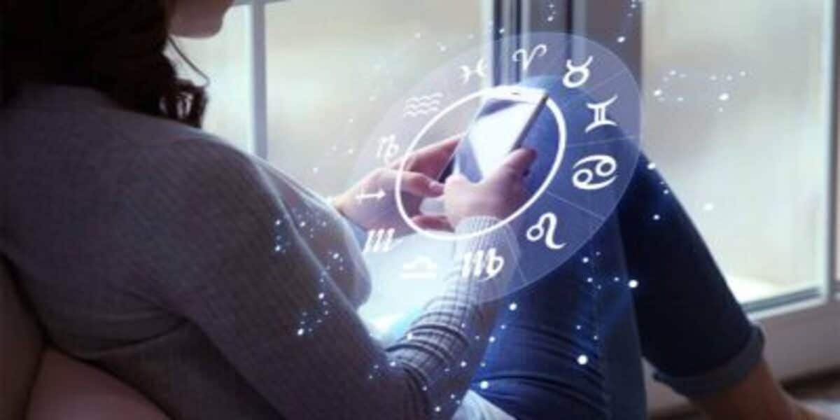 Pessoa mexendo no celular com desenho gráfico dos signos do zodiaco