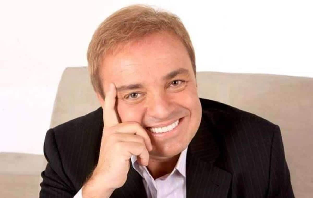 Apresentador de TV, Gugu Liberato, sorrindo e com a mão no rosto herança