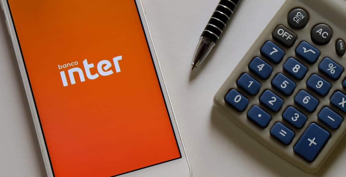 Aplicativo do banco Inter em celular com calculadora e caneta ao lado