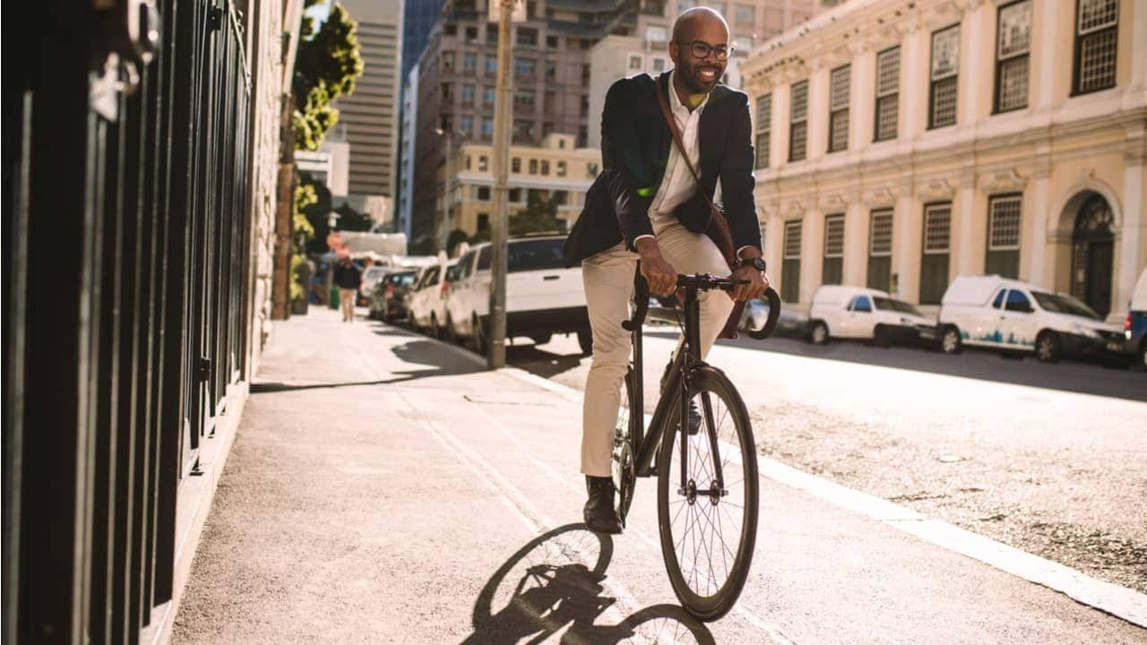 Na imagem, rapaz trajando roupas casuais, anda de bicicleta na rua.