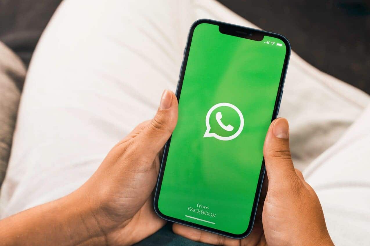 Imagem com duas mãos segurando um celular com o aplicativo WhatsApp aberto.